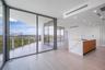 Floor-to-ceiling glass walls, expansive wraparound balcony, kitchen island with waterfall-edge stone countertop, wood-finish cabinetry, and neutral la