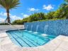 In-ground pool featuring a blue glass mosaic tile water wall, four integrated water features, a metal handrail, and stone-finish coping