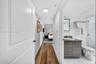 Wood-finish flooring throughout, bathroom featuring a vanity with dark-tone cabinetry, integrated sink, and an illuminated mirror, and a walk-in showe