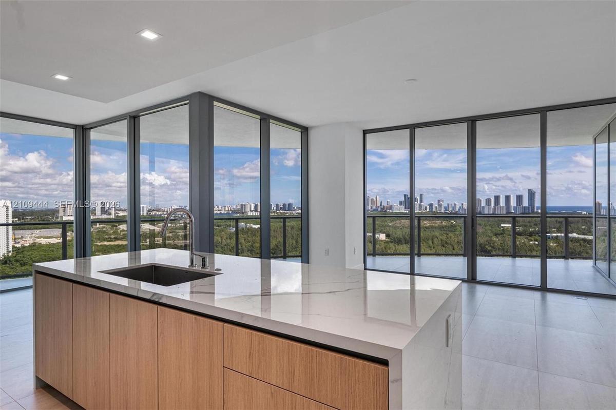 Kitchen island featuring waterfall-edge stone countertops, undermount sink, gooseneck faucet, and wood-finish cabinetry, set against floor-to-ceiling 