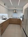 Modern kitchen featuring wood-finish cabinetry, solid-surface countertops, undermount sink with gooseneck faucet, stainless steel range hood, and line