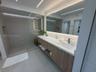 Floating wood-finish vanity with a white countertop and integrated sink, frameless glass walk-in shower with horizontal tile wall detailing, and a lar