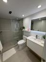 Walk-in shower with horizontal tile surround and glass partition, floating vanity featuring a rectangular integrated sink, white countertop, and LED-b