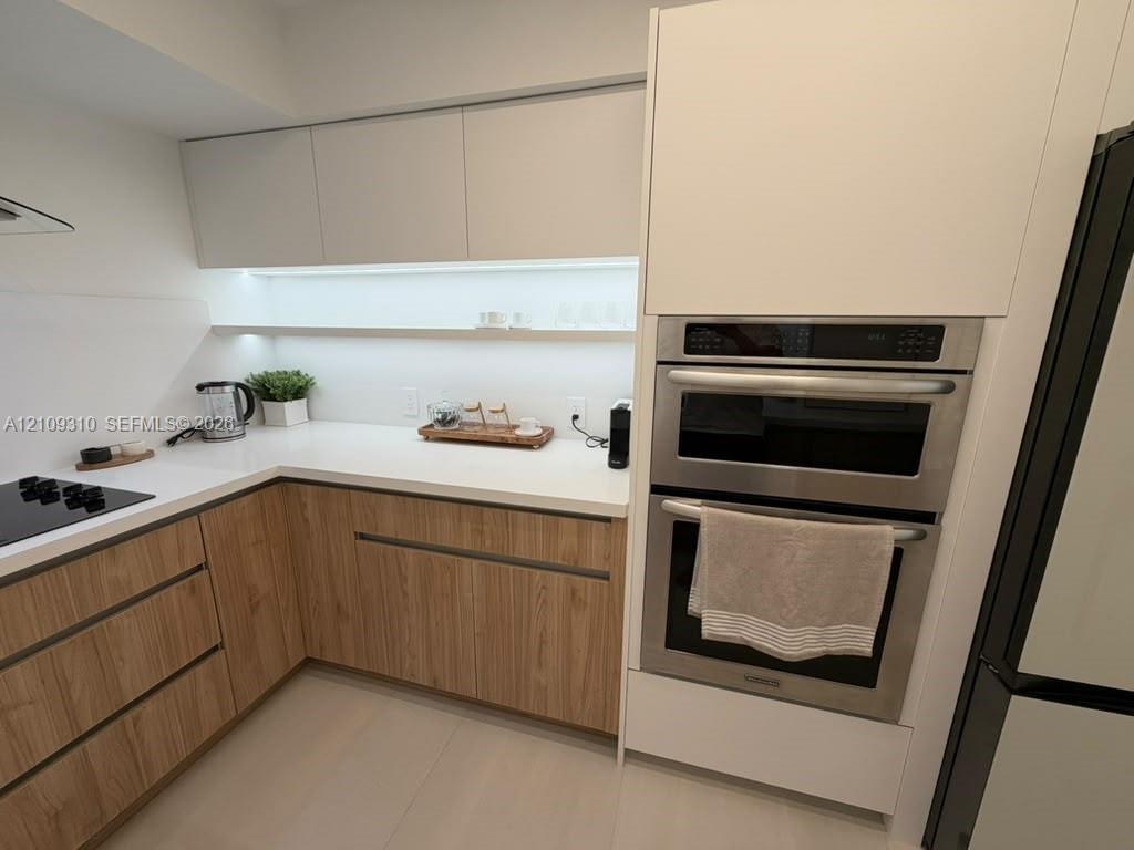 Kitchen featuring two-tone cabinetry with wood-finish lower units, white upper cabinets, white solid-surface countertops, integrated under-cabinet lig