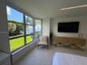 Floor-to-ceiling windows featuring waterfront scenery, neutral tile flooring, recessed linear lighting, and wall-mounted television console