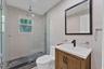 Bathroom featuring a wood-finish vanity with an integrated sink, matte black faucet, walk-in shower with a glass enclosure, pebble-tile flooring, and 
