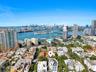 Aerial perspective of the coastal cityscape featuring a prominent skyline, expansive waterway, marinas, high-rise architecture, and mature canopy foli