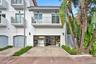 Stucco exterior featuring dual-level metal balconies, terracotta-style roof tile accents, a private herringbone-patterned paver driveway, and an attac