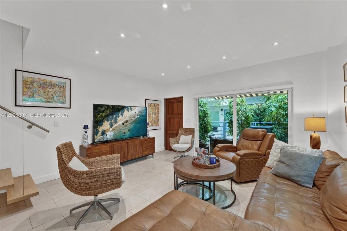 Large-format tile flooring, recessed ceiling lighting, sliding glass door with exterior access, and a floating wood-tread staircase with a glass panel