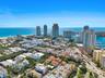 Aerial perspective of a coastal urban landscape featuring high-rise towers, proximity to the shoreline, a marina, and dense metropolitan infrastructur