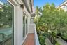 Exterior balcony featuring terracotta tile flooring, metal railing, stucco wall finish, and wall-mounted exterior lighting