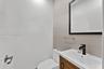 Vanity with a wooden cabinet base and integrated rectangular basin, matte black faucet, framed mirror, and textured tile wall accents
