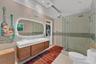 Floating wood-finish vanity with a white countertop and integrated sink, illuminated irregular-shaped vanity mirror, glass-enclosed shower with pebble