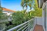 Outdoor balcony featuring red tile flooring, horizontal metal railings, and mature palm tree landscaping