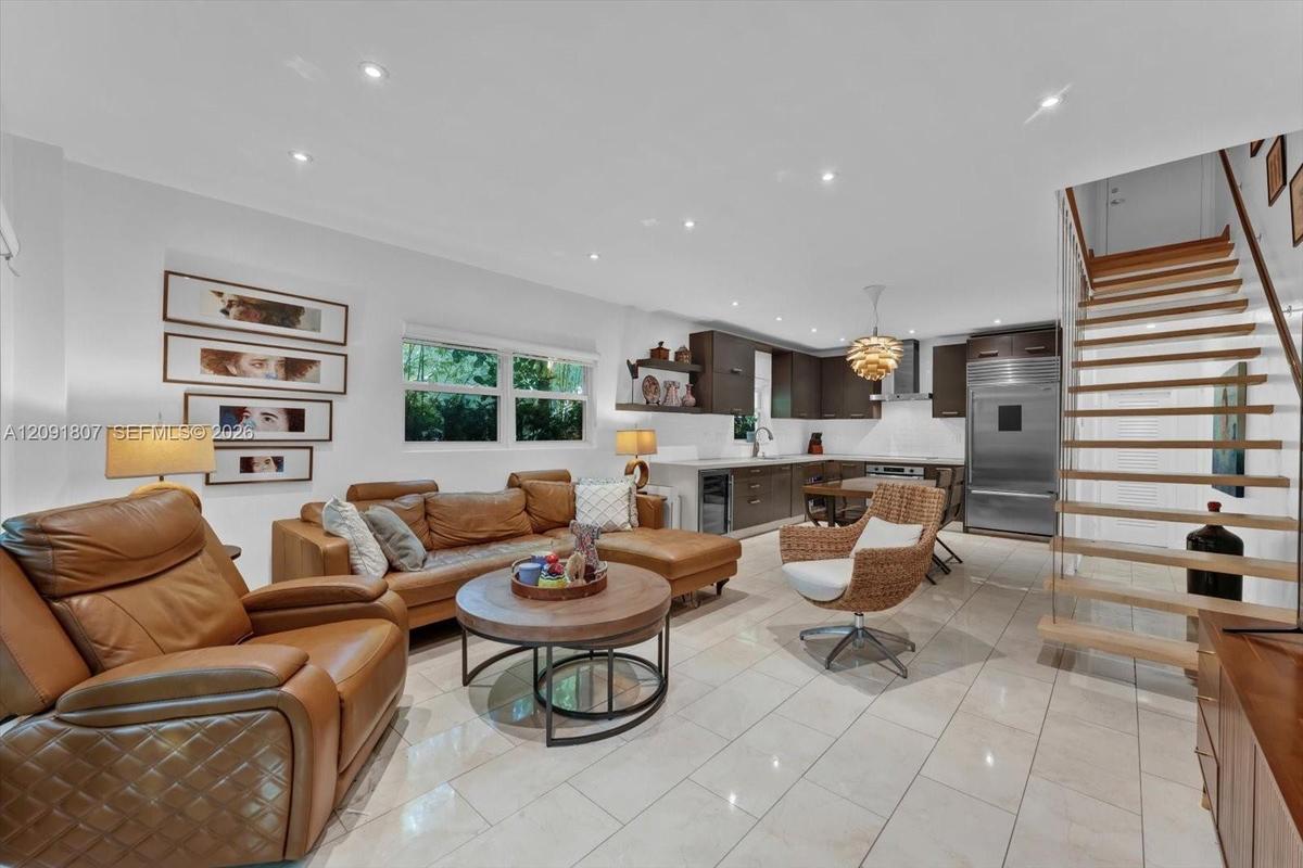 Open-concept living space featuring large-format tile flooring, recessed lighting, and a staircase with floating wood treads and cable railing