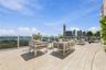 Expansive outdoor terrace featuring light-toned tile flooring, a glass panel railing, and a cityscape and water backdrop