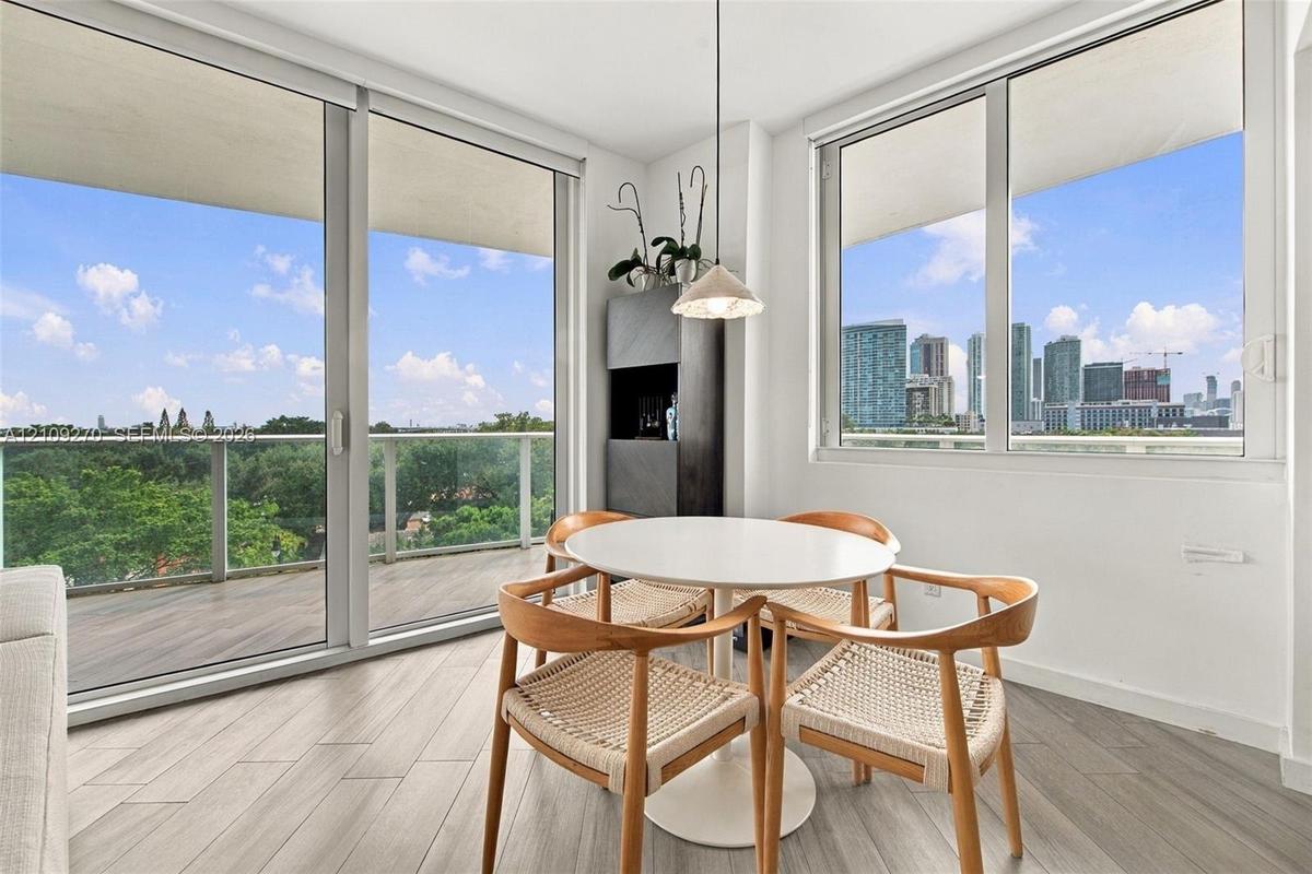 Floor-to-ceiling windows, wood-finish tile flooring, recessed balcony with glass railing, and a pendant light fixture