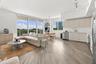 Open-concept main living area featuring wood-finish flooring, floor-to-ceiling glass sliding doors, flat-panel cabinetry, stainless steel appliances, 