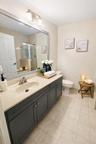 Bathroom featuring a vanity with dark cabinetry, a neutral countertop, an integrated oval sink, a wall-to-wall mirror, and tile flooring
