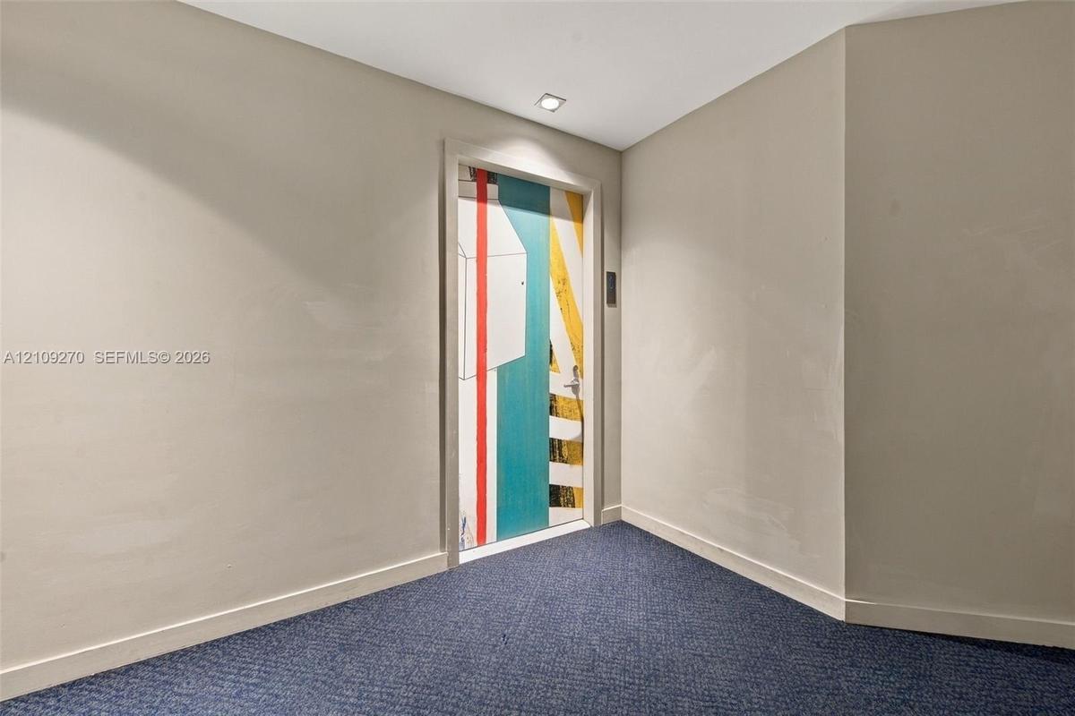 Neutral wall finishes, recessed ceiling lighting, and blue textured carpeting featuring a door with a custom geometric, multi-color graphic finish