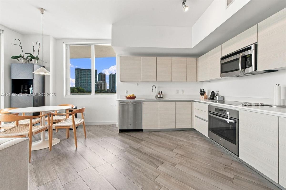 Kitchen featuring light-toned cabinetry, stainless steel appliances, wood-finish flooring, and expansive windows