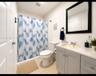 Bathroom featuring a vanity with light gray shaker-style cabinetry, a solid surface countertop, an integrated rectangular sink, a black-framed mirror,