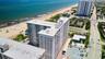 High-rise structure featuring exterior balconies, a flat roofline, and covered surface parking, situated along a coastal coastline