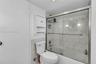 Bathroom featuring a white toilet, wall-mounted storage cabinet, and a bathtub with a glass sliding enclosure