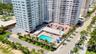 High-rise residential building featuring an outdoor swimming pool, paved surface parking, and perimeter landscaping with palm trees