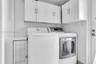 Laundry area featuring white shaker-style wall-mounted cabinetry, built-in lower storage with louvered door, and stainless steel hardware