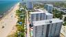 Aerial perspective of high-rise building with balcony access, positioned along the coastline featuring sandy shoreline and oceanfront proximity