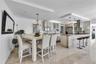 Open-concept kitchen featuring light wood cabinetry, stone-clad kitchen island, stainless steel appliances, tiered tray ceilings, and neutral tile flo
