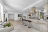 Open-concept kitchen featuring stone-clad breakfast bar, stainless steel chimney-style range hood, light-toned cabinetry, and tile flooring
