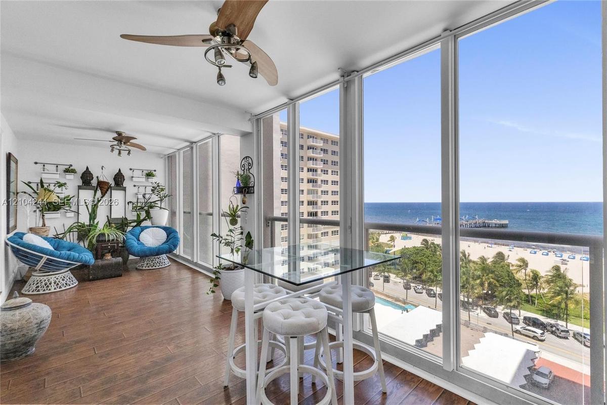 Enclosed sunroom featuring floor-to-ceiling glass panel walls, and dual ceiling fans, accented by a panoramic ocean backdrop