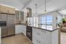 Kitchen featuring stone countertops, stainless steel appliances, a stainless steel range hood, glass-front cabinetry, and pendant lighting