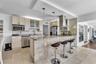 Kitchen featuring stone-clad breakfast bar, stone countertops, stainless steel appliances, cabinet-fronted upper storage with glass inserts, and two p