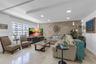 Living area featuring a textured stone accent wall, large-format tile flooring, a recessed tray ceiling with integrated lighting, and expansive window