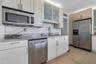 Kitchen featuring light-toned cabinetry with glass-fronted uppers, stone-finish countertops, stainless steel appliances, and tile flooring