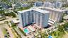 High-rise residential building featuring multiple private balconies, a ground-level swimming pool, on-site parking, and immediate proximity to coastal