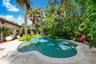 Custom-shaped swimming pool with stone coping, concrete decking, and established tropical landscaping