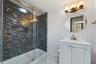 Bathroom featuring a walk-in shower with glass sliding doors and multi-tonal linear tile surround, brass-finish fixtures, white vanity cabinet with an