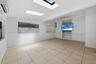 Large room featuring neutral tile flooring, dual skylights, custom built-in cabinetry, horizontal window blinds, and a ceiling fan