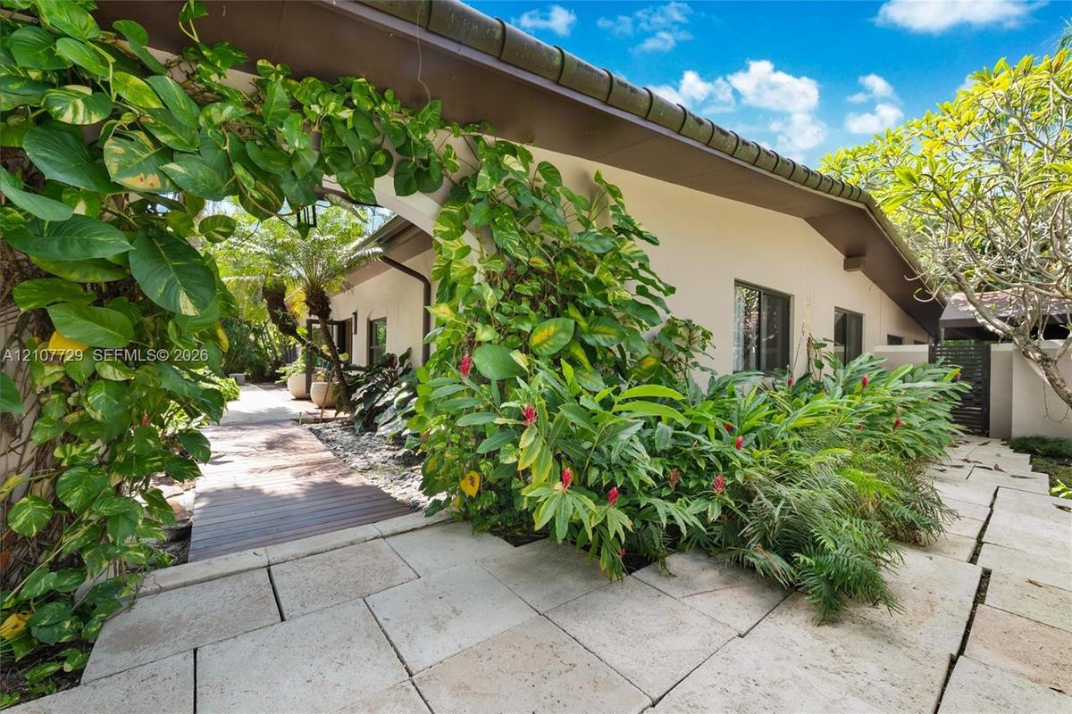 Exterior entrance featuring large-format light stone pavers, a wood-plank walkway, and established tropical landscaping