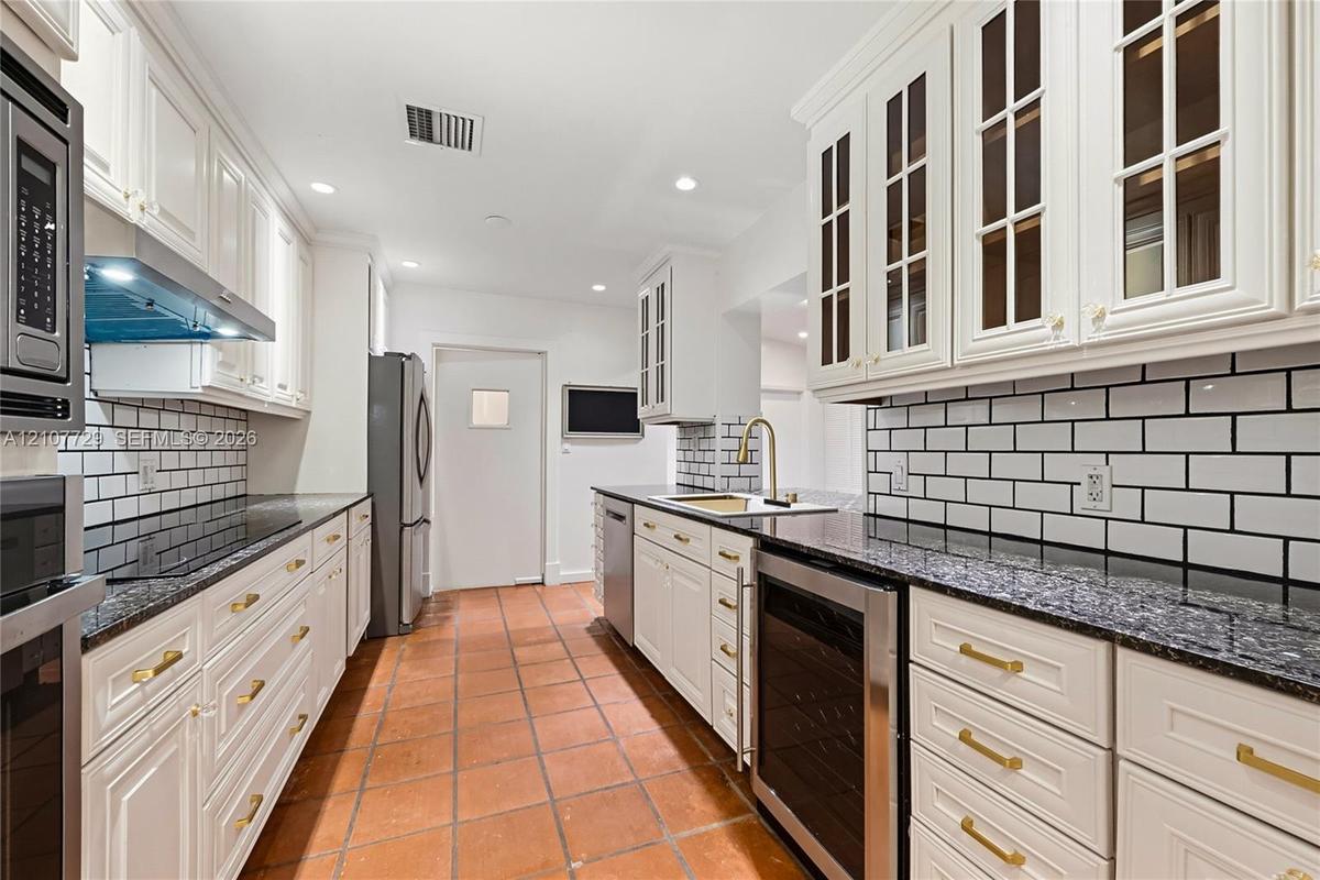 Kitchen featuring white cabinetry with glass-panel upper doors, dark stone countertops, subway tile backsplash, brass-tone hardware, and terra-cotta t