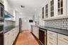 Kitchen featuring white cabinetry with glass-panel upper doors, dark stone countertops, subway tile backsplash, brass-tone hardware, and terra-cotta t