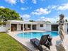 Backyard featuring a curved inground pool, expansive paver patio, covered porch with column supports, and manicured lawn