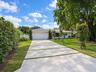 Single-story residence featuring a light-toned stucco exterior, a segmented concrete driveway, a multi-car garage, a tiled roof, and mature perimeter 