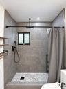 Walk-in shower featuring large-format grey tile surround, hexagonal floor tiling, a ceiling-mounted rainfall showerhead, and matte black plumbing fixt