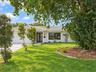 Single-story residence featuring a white painted brick exterior, tile roof, expansive front lawn, landscaped mulch garden beds with stone border, and 