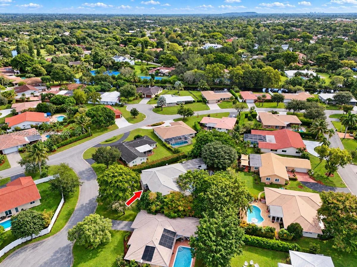 Aerial perspective of a suburban neighborhood featuring tree-lined streets, landscaped lots, and proximity to green space
